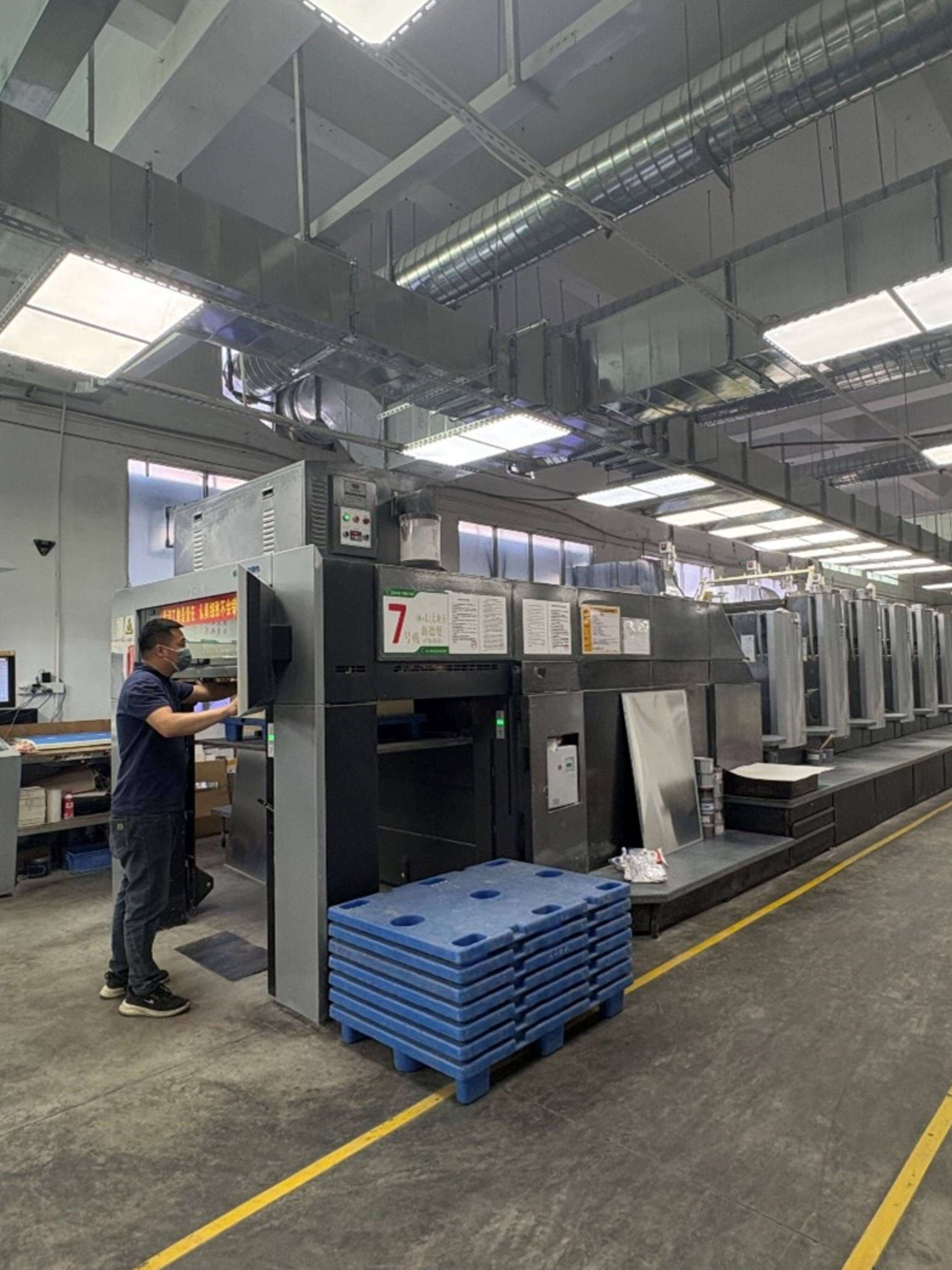 Worker operating multi-color printing press - precision puzzle manufacturing